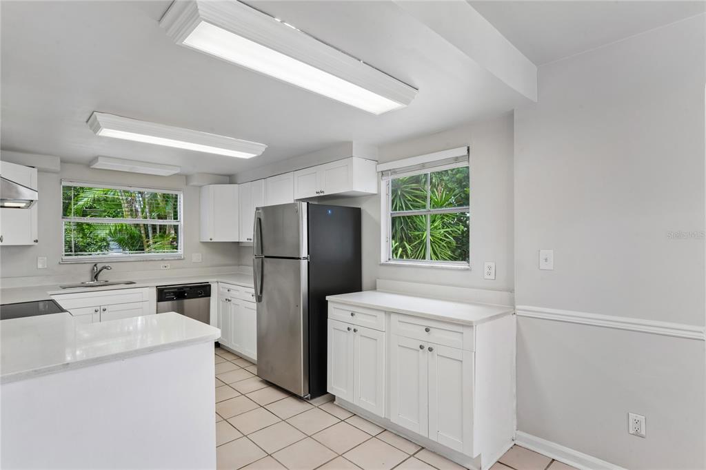 A kitchen features white cabinets, stainless steel appliances, tile flooring, and two windows — 14623 SUNSET DRIVE, LARGO, FL