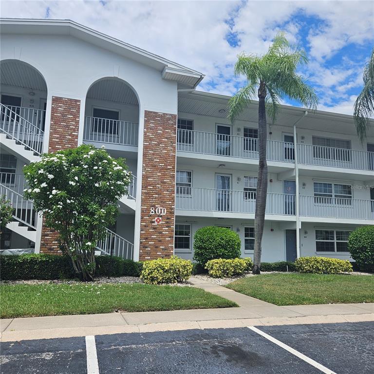 A three-story apartment building with a brick facade, white balconies, and a tall palm tree — 802 BRANDY WINE DRIVE, LARGO, FL