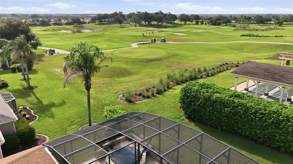 An elevated view of a screened-in patio overlooking a golf course with a pond — 1064 ALCOVE LOOP, THE VILLAGES, FL