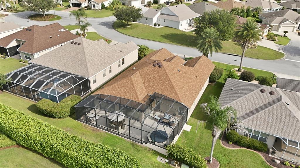 An aerial view shows three suburban houses with screened-in pool lanais and manicured lawns — 1064 ALCOVE LOOP, THE VILLAGES, FL