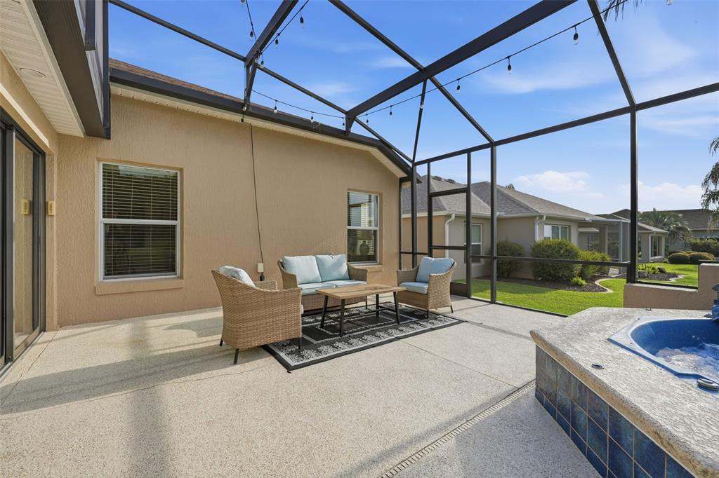 A screened-in patio features a hot tub, outdoor furniture, and a concrete floor — 1064 ALCOVE LOOP, THE VILLAGES, FL