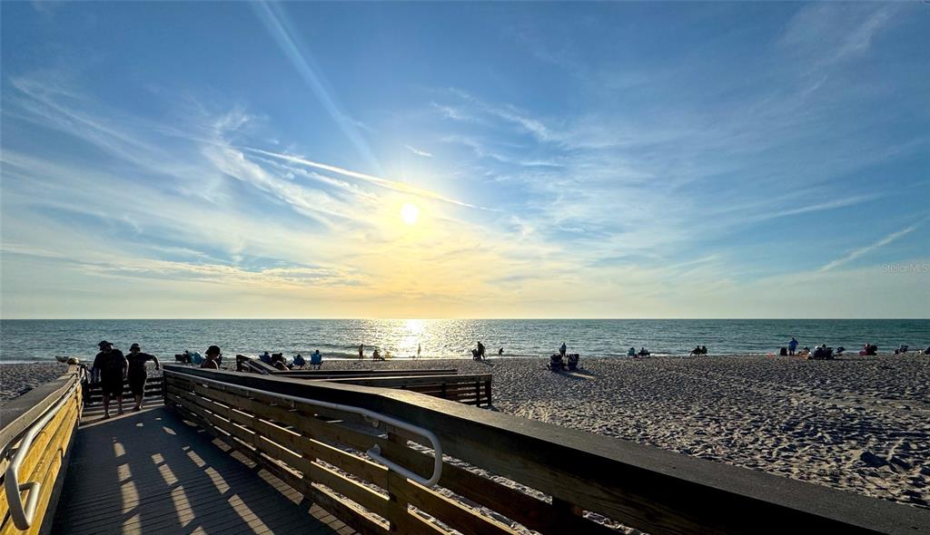 A wooden boardwalk leads to a sandy beach under a bright, sunny sky — 5881 SUNFLOWER ROAD, VENICE, FL