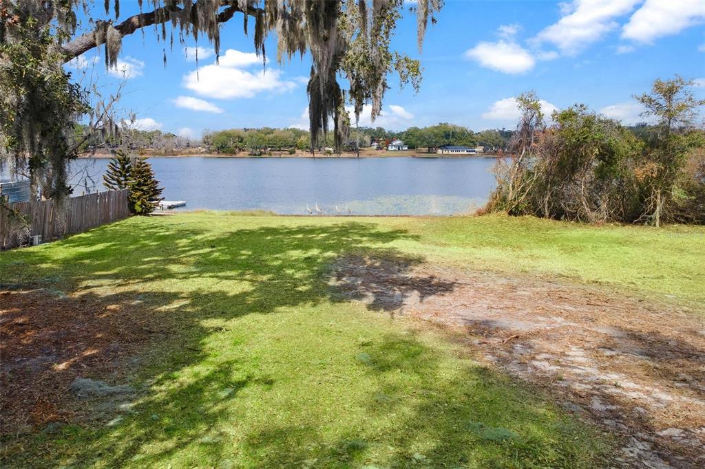 A grassy backyard slopes down toward a lake with trees and a wooden fence — 0 WILSON PARRISH ROAD, UMATILLA, FL