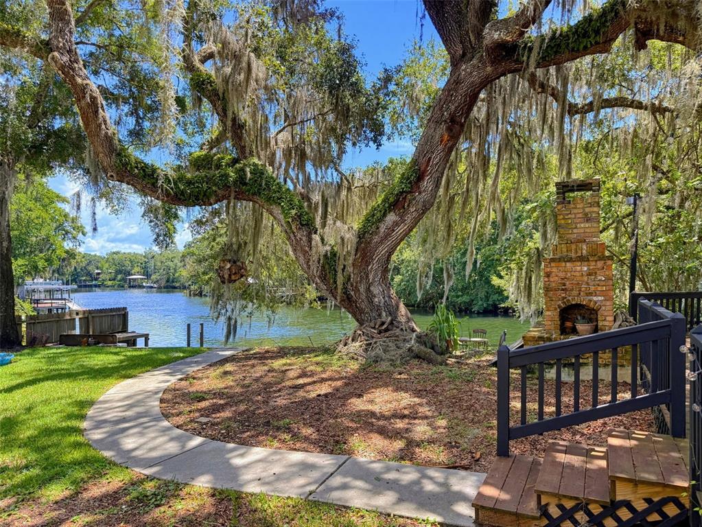 A large oak tree with Spanish moss stands near a brick fireplace and waterfront view — 5415 RIVERSIDE DRIVE, YANKEETOWN, FL