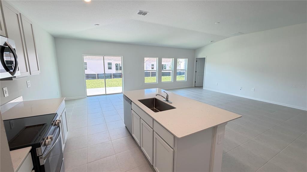 A kitchen with a central island, stainless steel appliances, and tile flooring opens to a living area — 4585 GOLDEN KNIGHT BOULEVARD, KISSIMMEE, FL