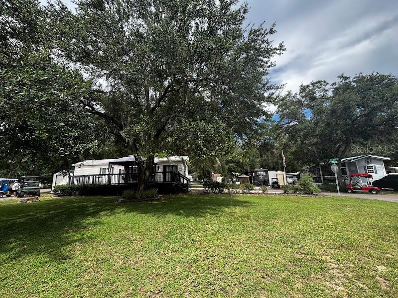 A mobile home with a wooden deck sits on a grassy lot under large trees — 14104 253RD AVENUE ROAD NE UNIT 398, FORT MC COY, FL