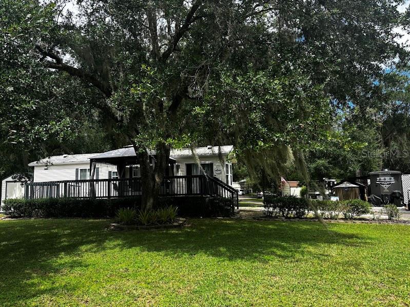 A white mobile home with a large wooden deck sits under a canopy of trees — 14104 253RD AVENUE ROAD NE UNIT 398, FORT MC COY, FL