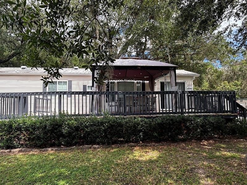A light-colored mobile home features a large wooden deck with a covered gazebo — 14104 253RD AVENUE ROAD NE UNIT 398, FORT MC COY, FL