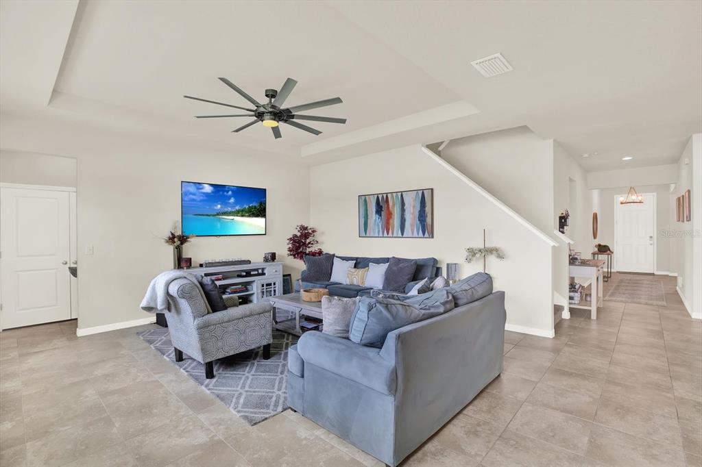 A living room features a blue sectional sofa, a patterned armchair, and a ceiling fan — 6723 DEVESTA LOOP, PALMETTO, FL