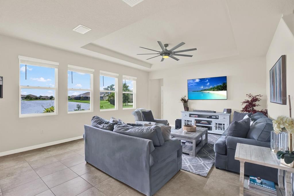 A living room with gray sofas, a ceiling fan, and windows overlooking a lake — 6723 DEVESTA LOOP, PALMETTO, FL