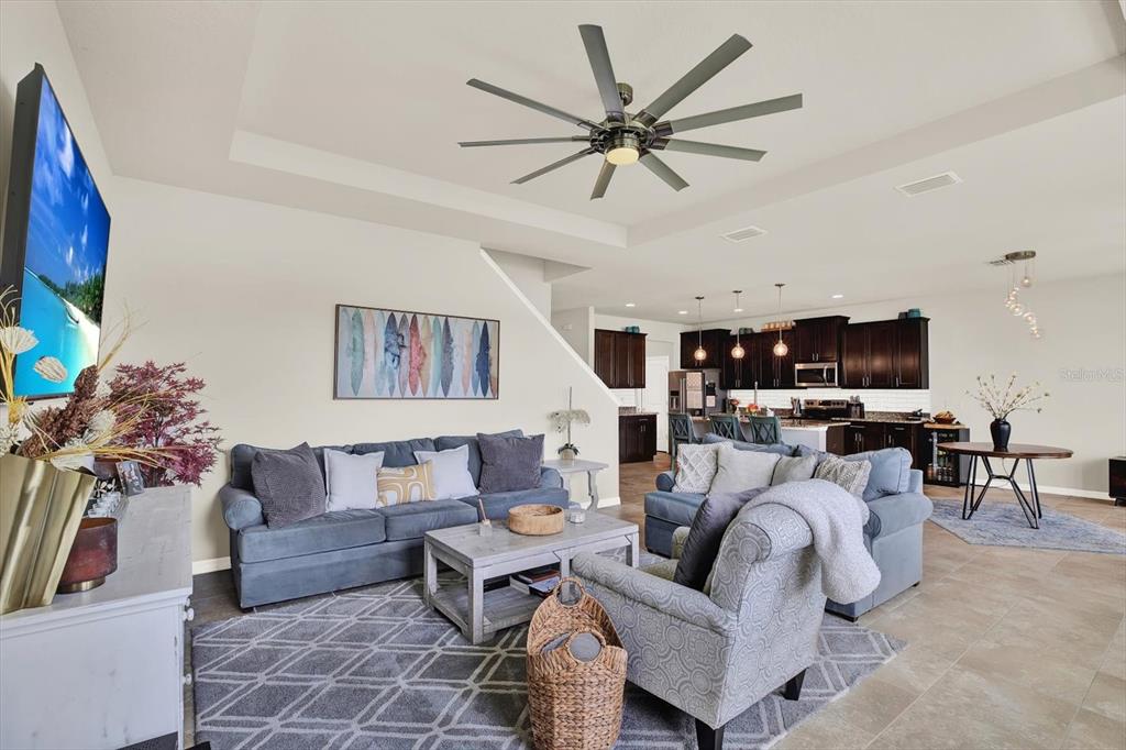 An open-concept living room features a blue sofa, gray armchair, and a kitchen in back — 6723 DEVESTA LOOP, PALMETTO, FL