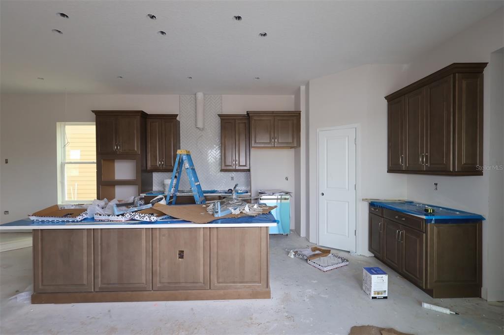 An unfinished kitchen features dark wood cabinets, a large island, and light-colored wall paint — 3090 BONFIRE PATH, ST CLOUD, FL