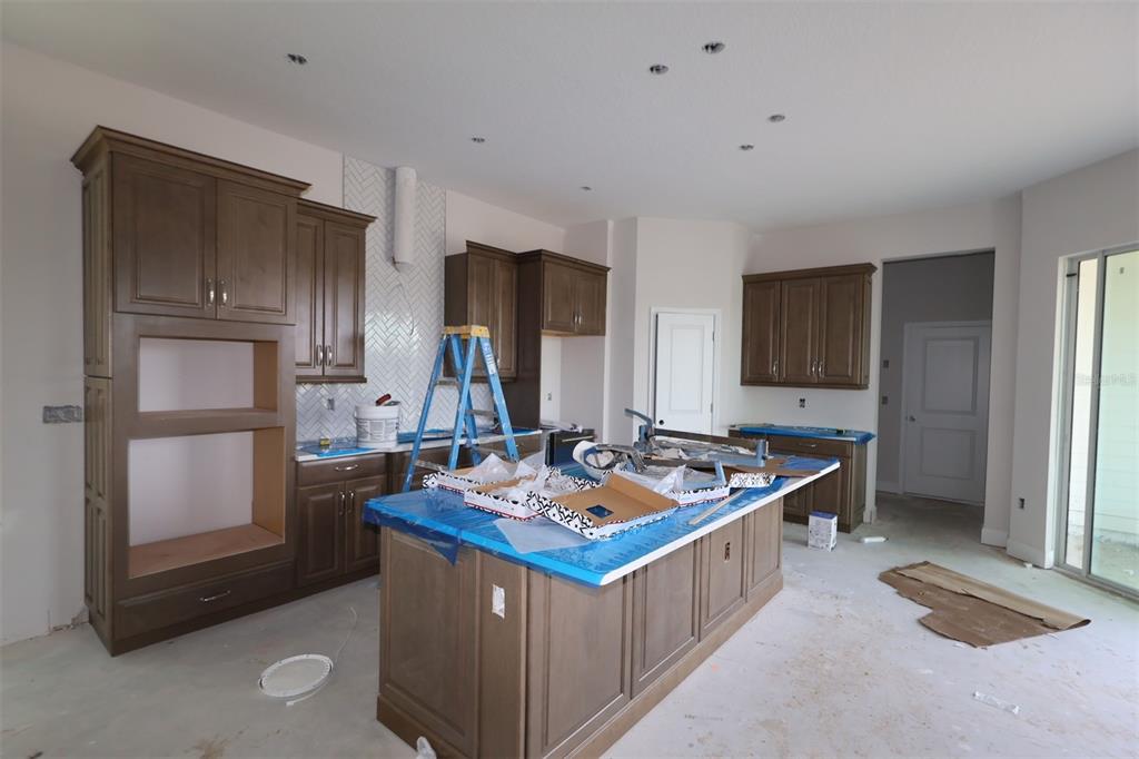 A kitchen under construction features brown cabinets, a large island, and a herringbone tile backsplash — 3090 BONFIRE PATH, ST CLOUD, FL