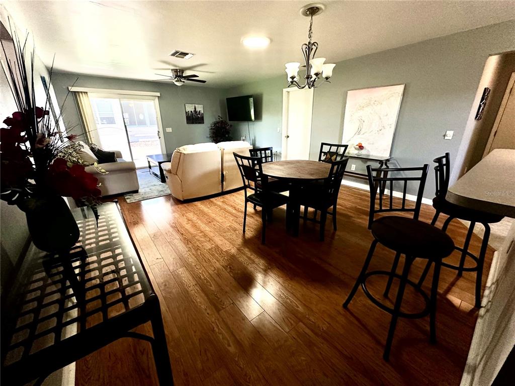 An open-concept living and dining area features wood-look flooring, a ceiling fan, and a chandelier — 8036 SE 175TH MALMAISON STREET, THE VILLAGES, FL