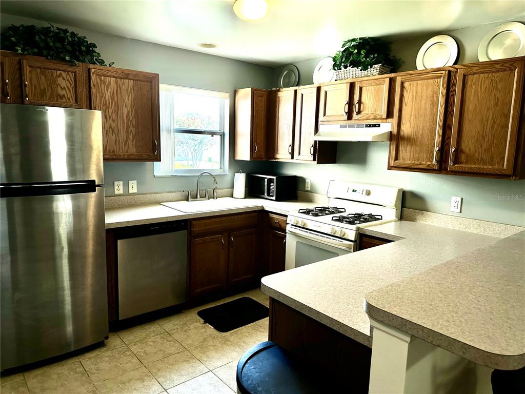 A kitchen features stainless steel appliances, wood cabinets, and light-colored countertops — 8036 SE 175TH MALMAISON STREET, THE VILLAGES, FL