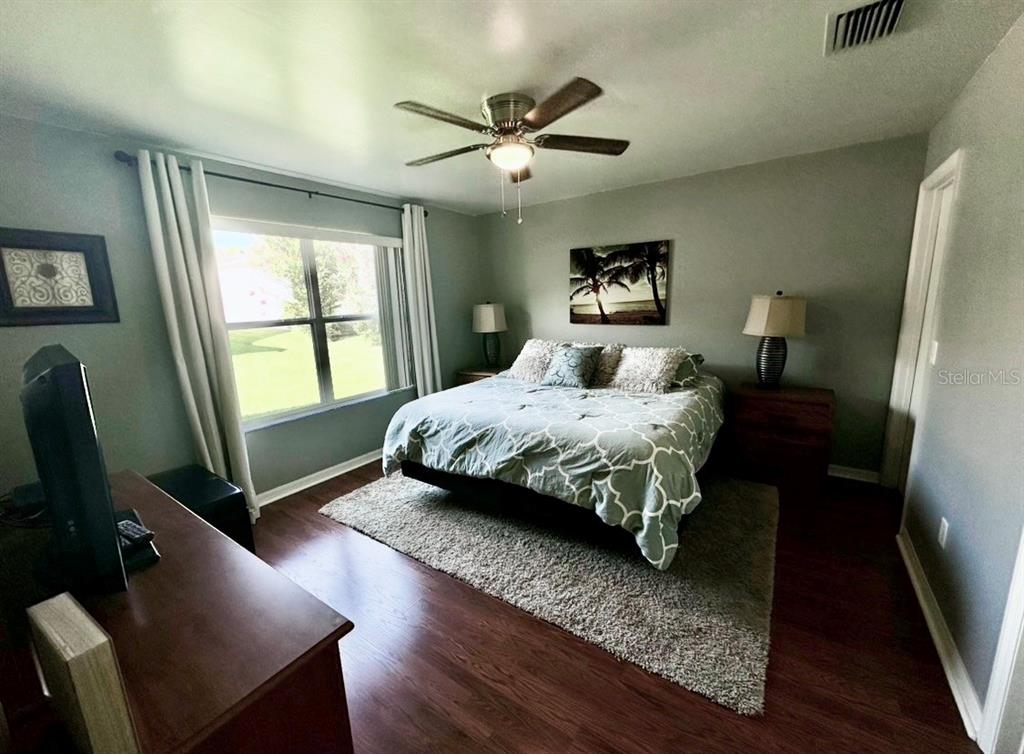 A bedroom features a bed with a patterned comforter, a ceiling fan, and wood flooring — 8036 SE 175TH MALMAISON STREET, THE VILLAGES, FL
