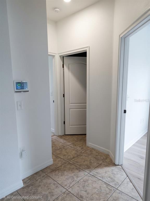 A hallway with tile flooring leads to two doorways and features a wall-mounted smart panel — 3998 PACENTE LOOP, WESLEY CHAPEL, FL