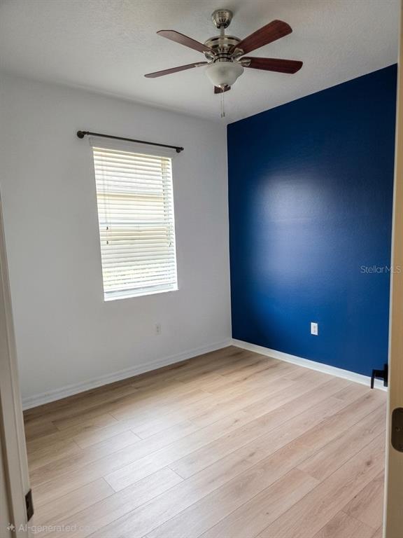 An empty bedroom features light wood-look flooring, a ceiling fan, and a dark blue accent wall — 3998 PACENTE LOOP, WESLEY CHAPEL, FL