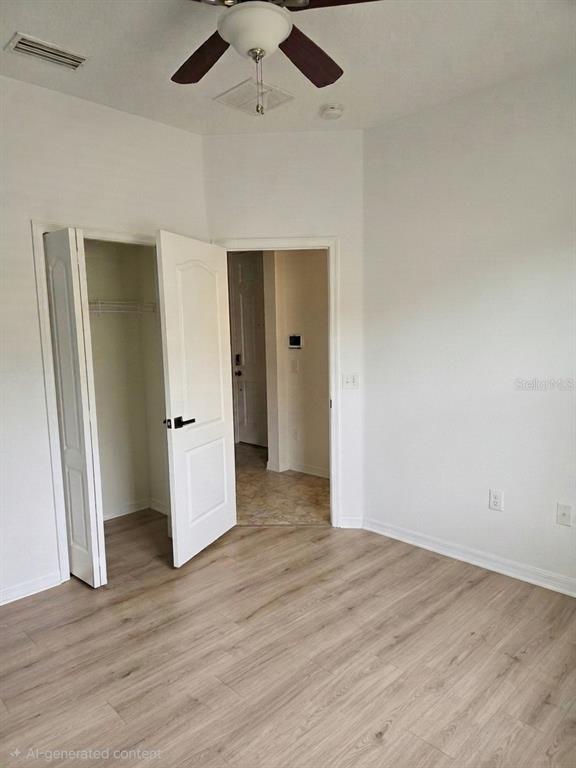 A bedroom features light wood-look flooring, a ceiling fan, and an open closet door — 3998 PACENTE LOOP, WESLEY CHAPEL, FL