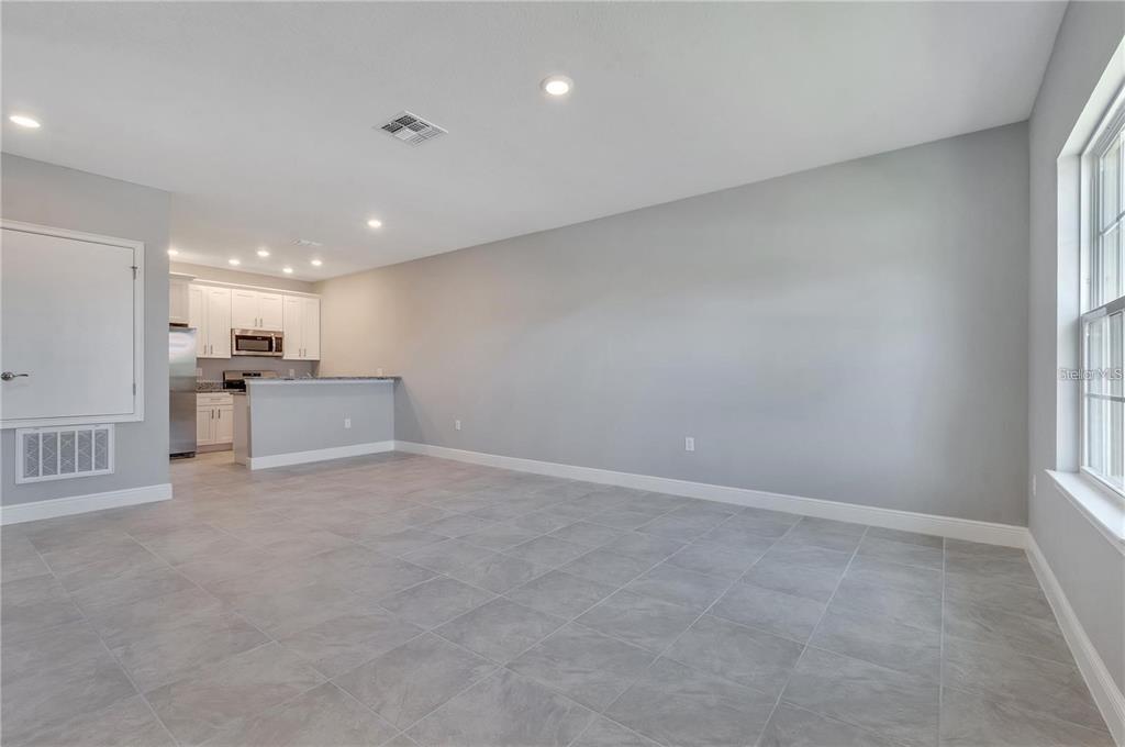 An open-concept living area features gray tile flooring, light gray walls, and an adjacent kitchen — 1795 CORIANDER DRIVE UNIT 1795, POINCIANA, FL
