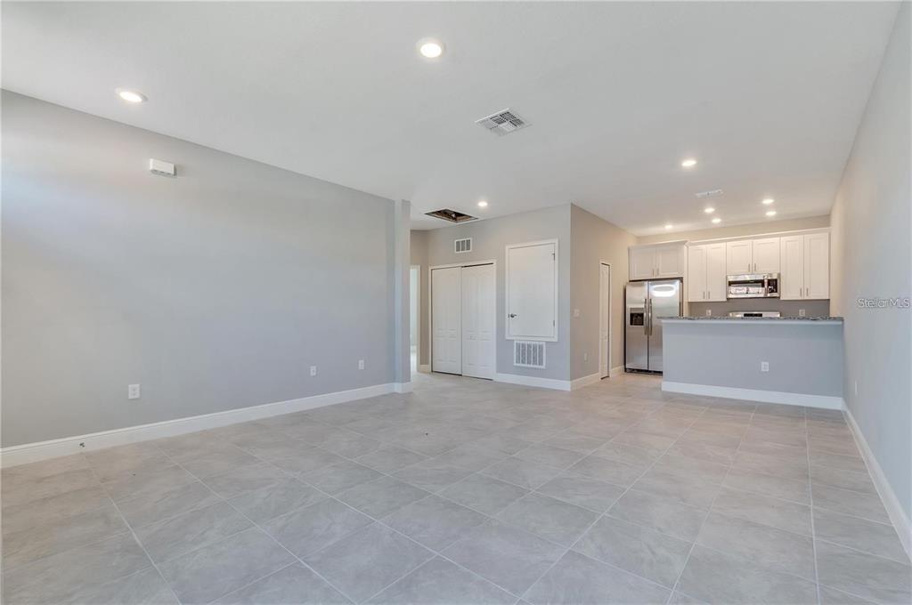 An open-concept living area features gray tile flooring, light gray walls, and an adjacent kitchen — 1795 CORIANDER DRIVE UNIT 1795, POINCIANA, FL