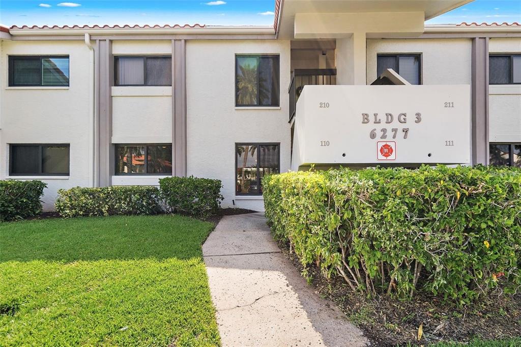 The exterior of a two-story apartment building features a concrete walkway and landscaped hedges — 6277 BAHIA DEL MAR BOULEVARD UNIT 110, ST PETERSBURG, FL