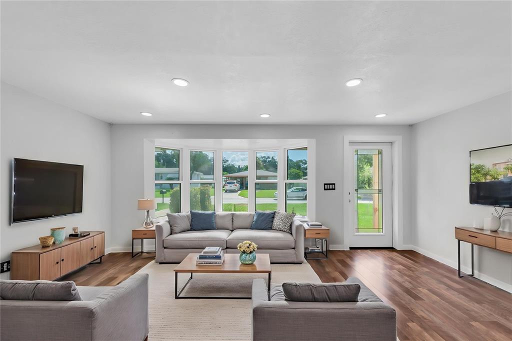 A living room features a gray sofa, two armchairs, a bay window, and wood flooring — 1516 COUNTRY LANE W, CLEARWATER, FL