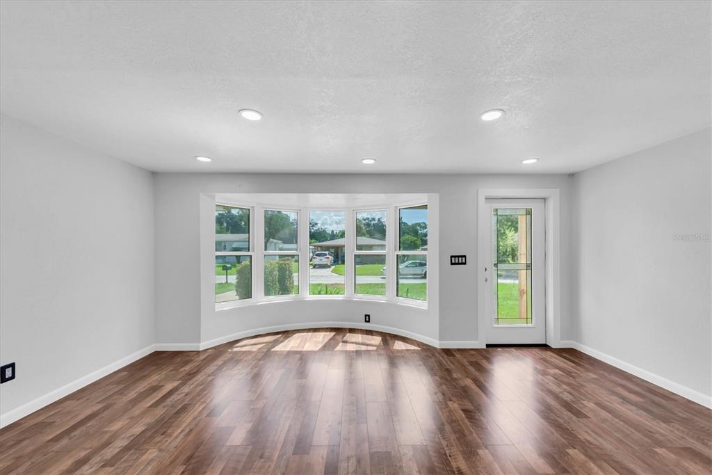 An empty room with wood-look flooring, recessed lighting, a bay window, and a glass door — 1516 COUNTRY LANE W, CLEARWATER, FL