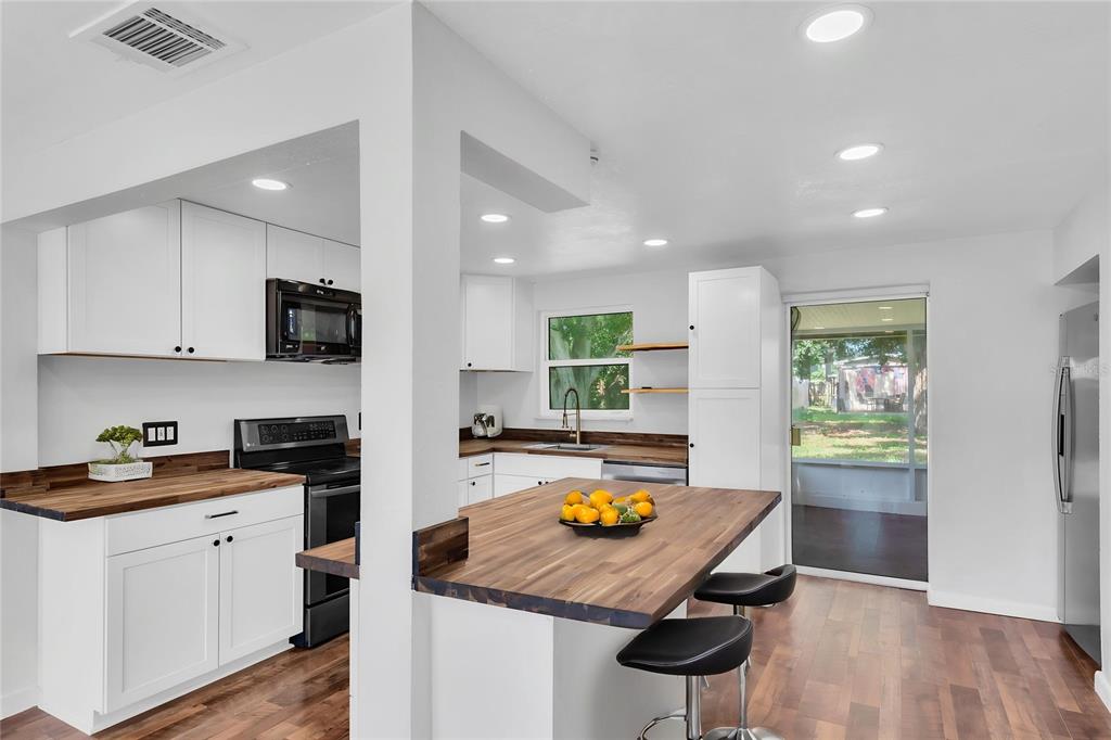 A modern kitchen features white cabinets, wood countertops, a central island, and stainless steel appliances — 1516 COUNTRY LANE W, CLEARWATER, FL