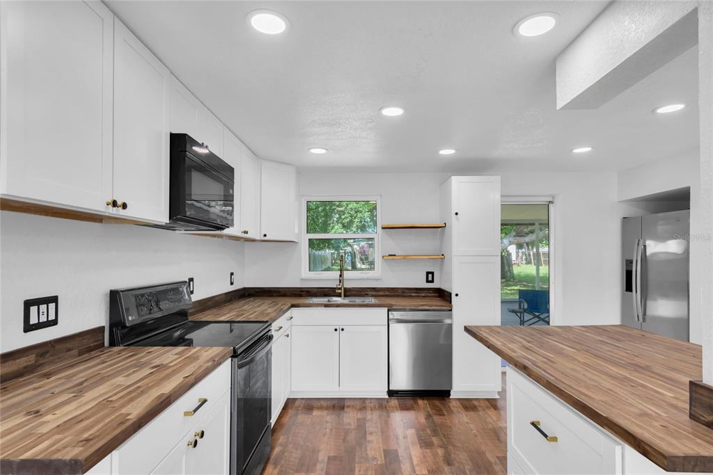 A kitchen features white cabinets, wood countertops, stainless steel appliances, and recessed lighting — 1516 COUNTRY LANE W, CLEARWATER, FL