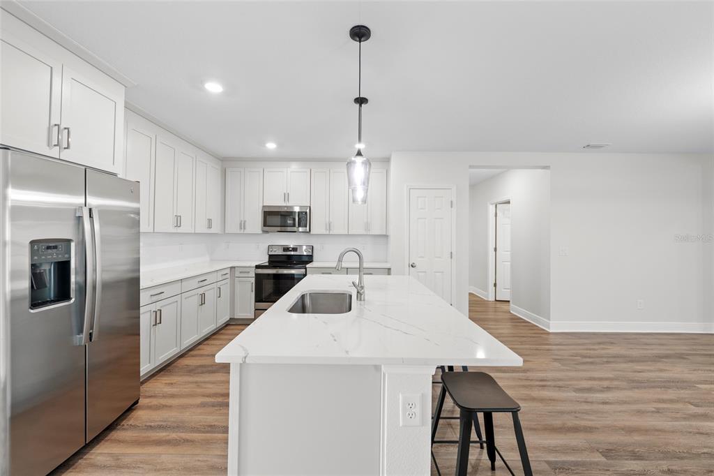 A modern kitchen features white cabinets, stainless steel appliances, and a marble-topped island with seating — 5540 PATANO LOOP, PALMETTO, FL