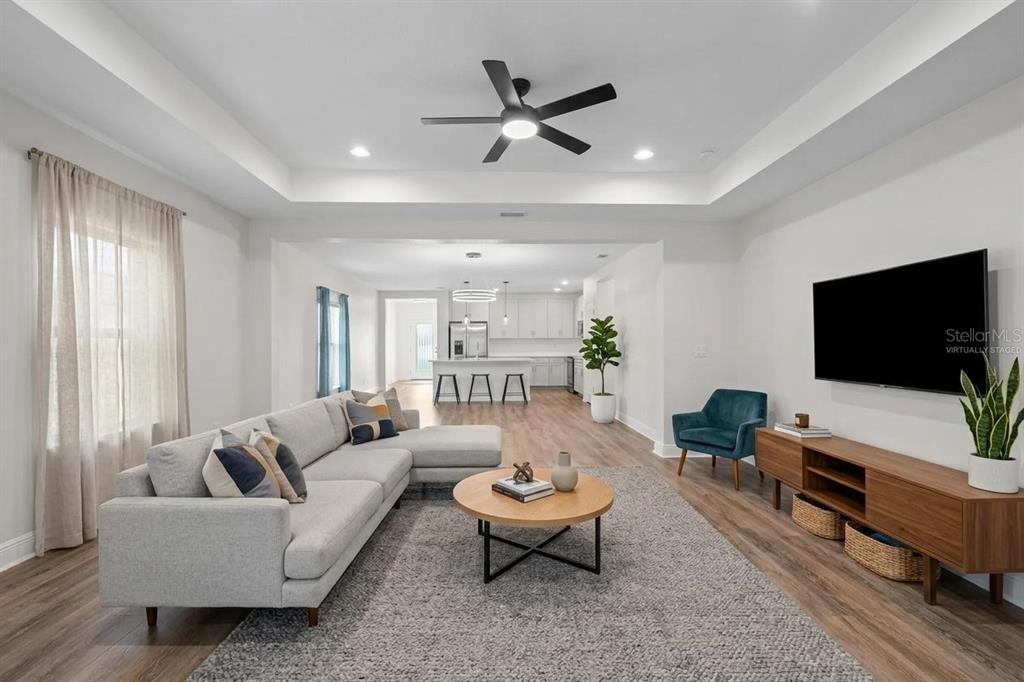 A living room with a gray sectional, wood coffee table, and television opens to a kitchen — 5540 PATANO LOOP, PALMETTO, FL