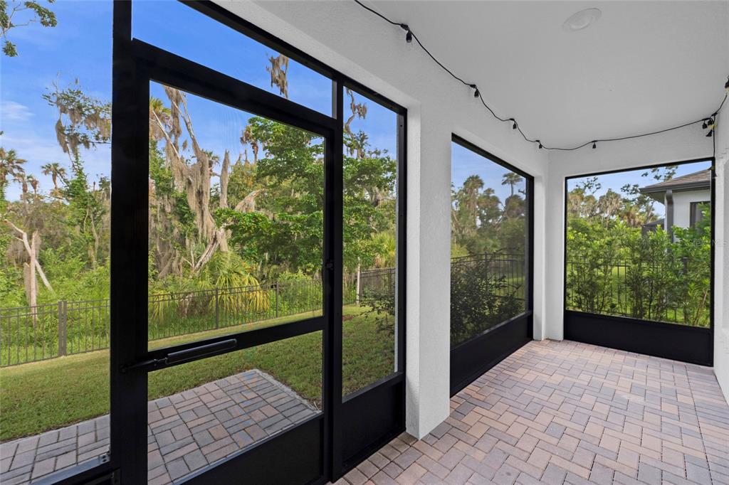 A screened-in patio with paver flooring overlooks a grassy yard and wooded area — 5540 PATANO LOOP, PALMETTO, FL