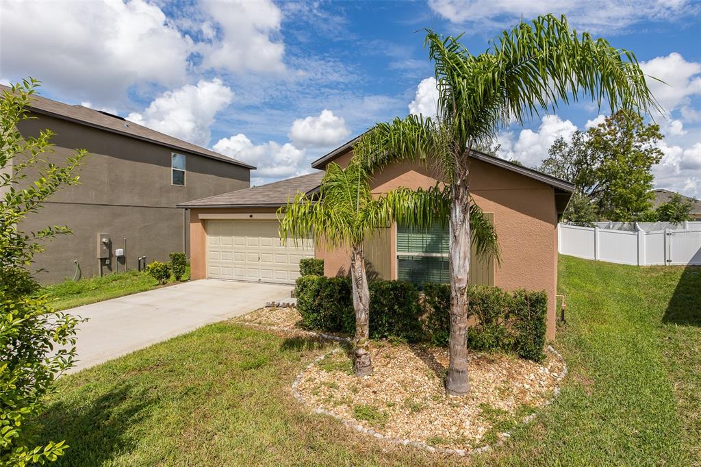 A single-story house with a tan stucco exterior, a two-car garage, and two palm trees — 518 ARGYLL DRIVE, SPRING HILL, FL