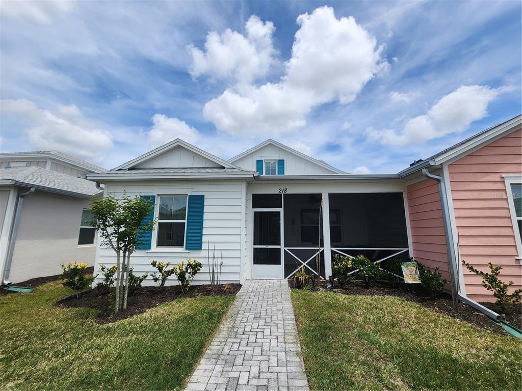 A white house with blue shutters and a screened-in front porch under a cloudy sky — 218 OCEAN HAMMOCK LOOP, DAYTONA BEACH, FL