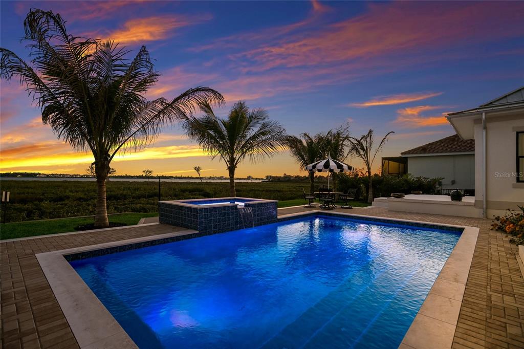 A swimming pool and spa overlook a waterfront view at sunset with palm trees nearby — 1517 4TH STREET E, PALMETTO, FL