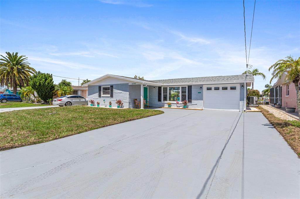 A single-story gray brick house features a white garage door and a paved driveway — 12700 5TH ISLE, HUDSON, FL