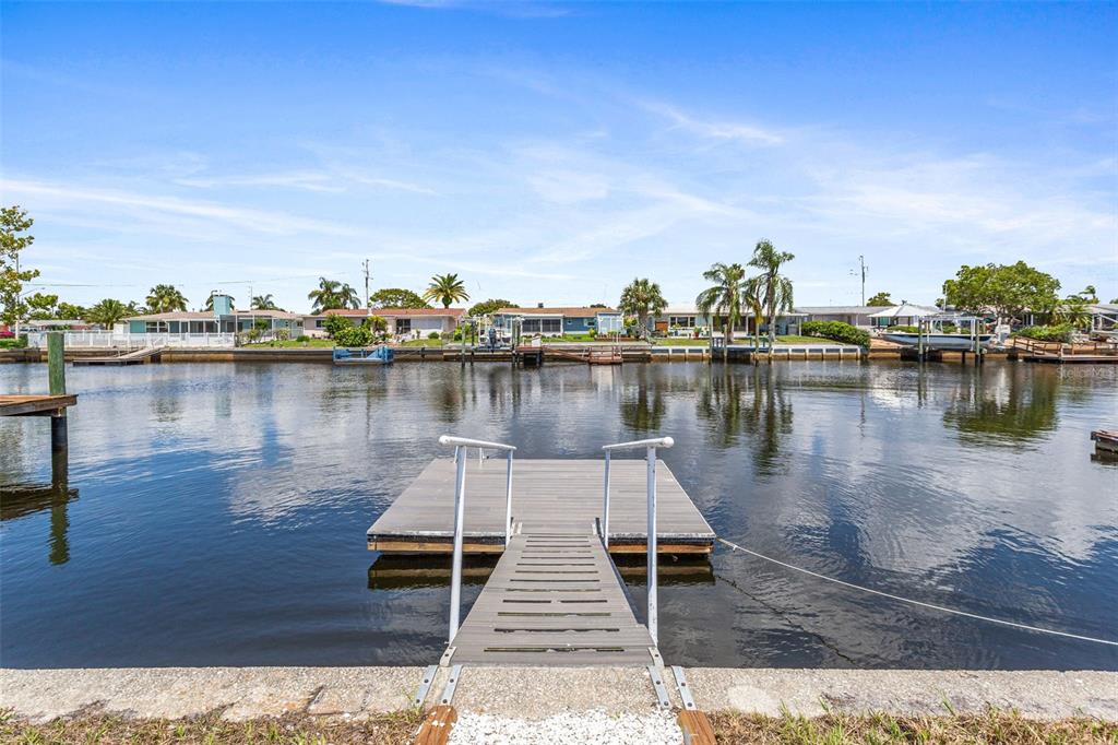 A floating dock with a ramp extends into a canal lined with residential homes — 12700 5TH ISLE, HUDSON, FL