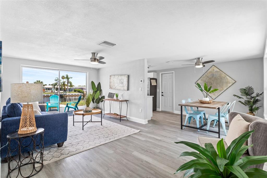 An open-concept living and dining area features light wood flooring, ceiling fans, and waterfront views — 12700 5TH ISLE, HUDSON, FL