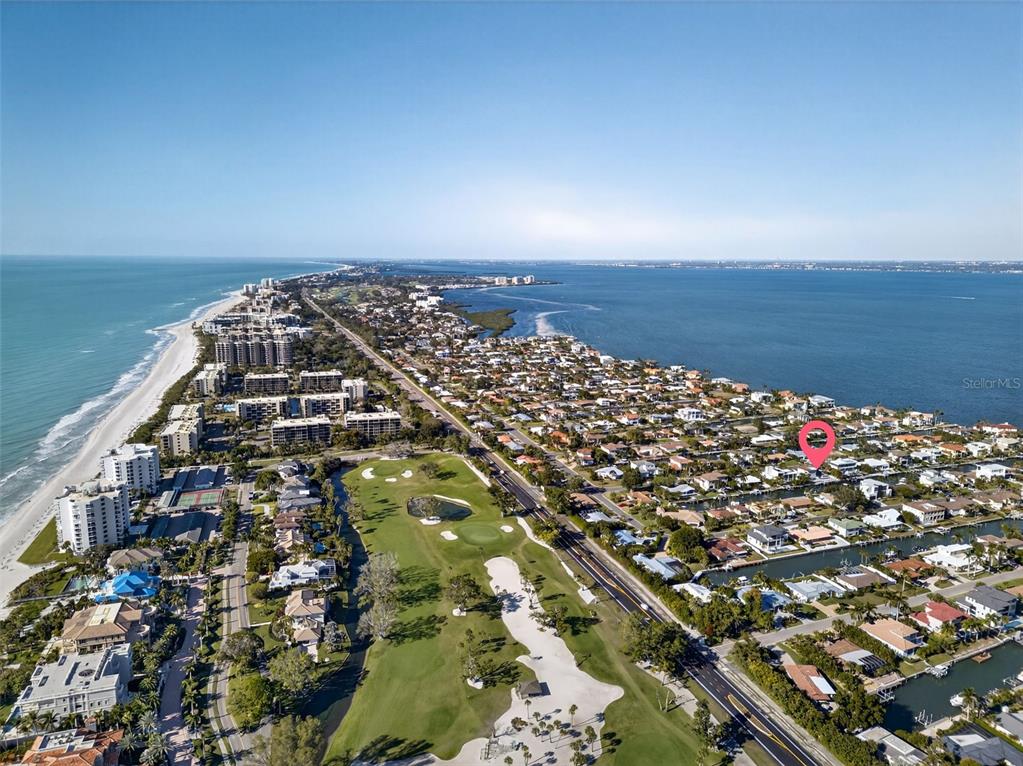 An aerial view shows a coastal neighborhood with a golf course, beach, and residential homes — 562 RANGER LANE, LONGBOAT KEY, FL