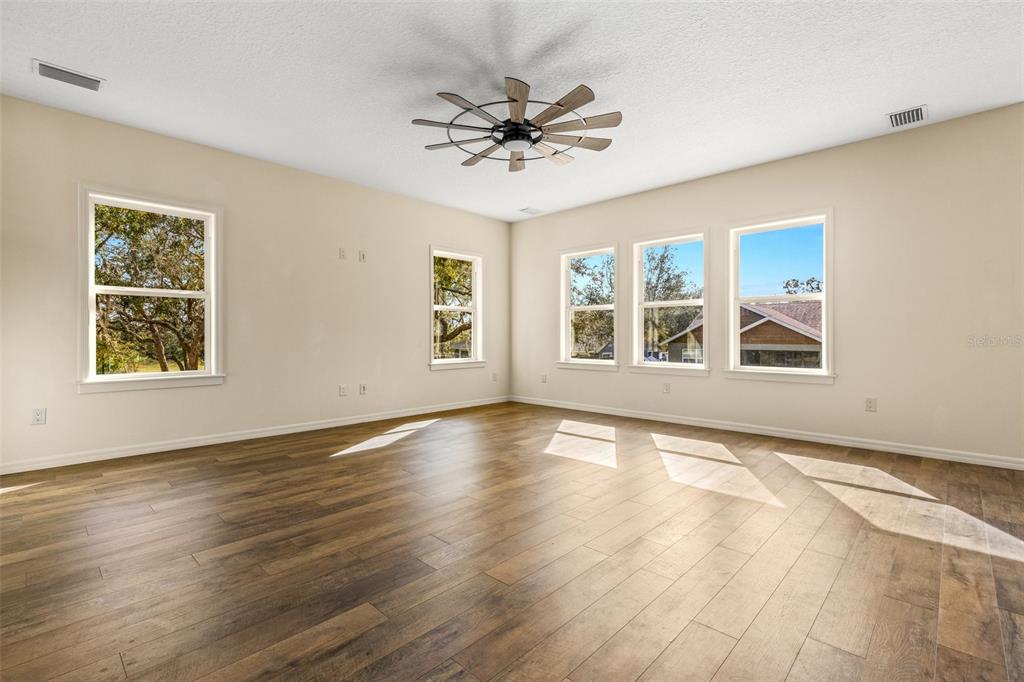 An empty living room features light-colored walls, wood-look flooring, a ceiling fan, and multiple windows — 5332 W WESTCHASE LOOP, LECANTO, FL