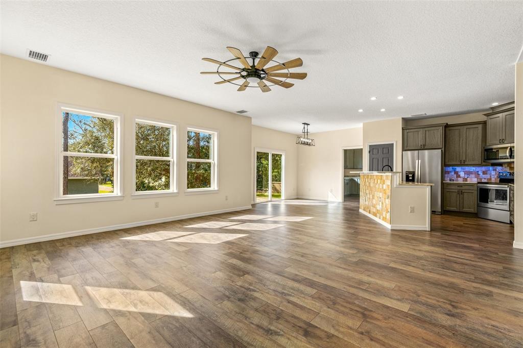 An open-concept living area features wood-look flooring, a ceiling fan, and an adjacent kitchen — 5332 W WESTCHASE LOOP, LECANTO, FL