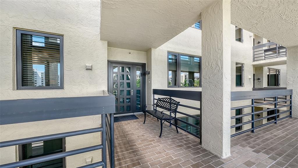 An outdoor walkway with a brick floor, metal railings, a bench, and a glass door — 1075 GULF OF MEXICO DRIVE UNIT 303, LONGBOAT KEY, FL
