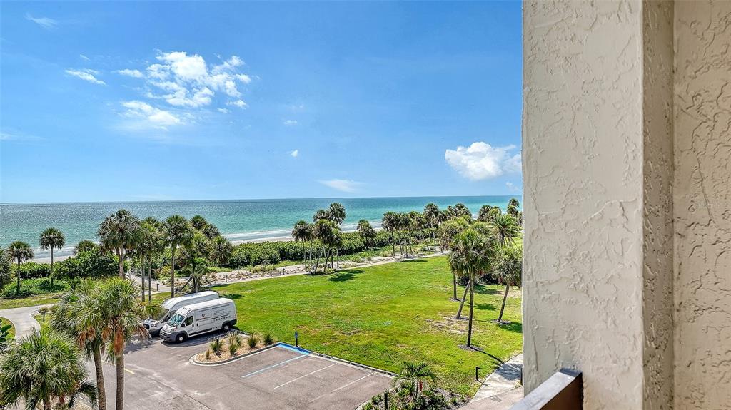 An elevated view from a balcony overlooking a grassy lawn, palm trees, and the ocean — 1075 GULF OF MEXICO DRIVE UNIT 303, LONGBOAT KEY, FL