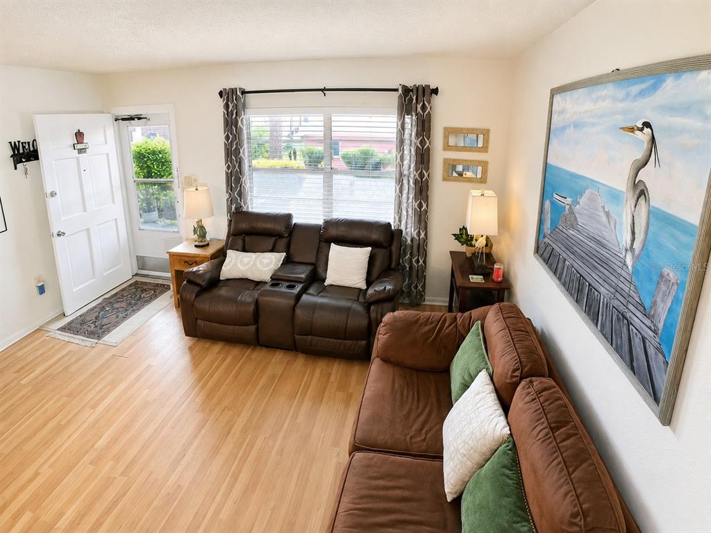 A living room features light wood flooring, two brown sofas, and a large heron wall painting — 4746 AZALEA DRIVE UNIT 109, NEW PORT RICHEY, FL