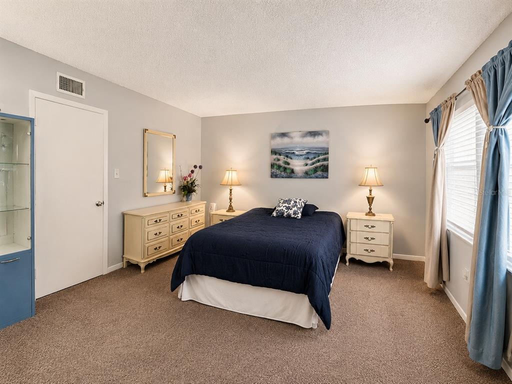 A bedroom features a dark blue bedspread, two matching nightstands, a dresser, and beige carpeting — 4746 AZALEA DRIVE UNIT 109, NEW PORT RICHEY, FL