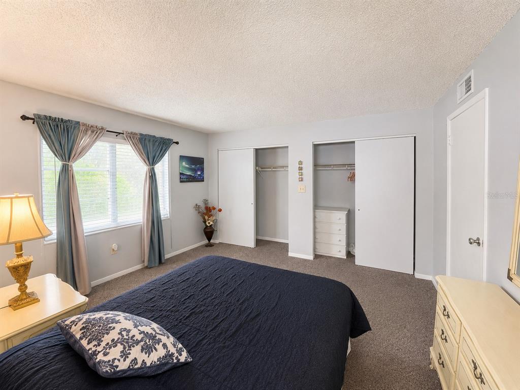 A bedroom features a dark blue bedspread, two closets with sliding doors, and a window — 4746 AZALEA DRIVE UNIT 109, NEW PORT RICHEY, FL