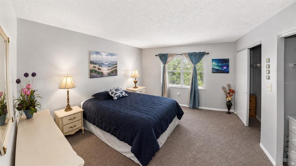 A bedroom features a dark blue bedspread, two nightstands with lamps, and a walk-in closet — 4746 AZALEA DRIVE UNIT 109, NEW PORT RICHEY, FL