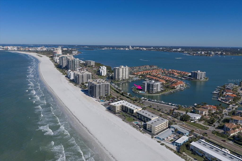 An aerial view shows a coastal beach, high-rise condominiums, and a bay with a marina — 1651 SAND KEY ESTATES COURT UNIT 28, CLEARWATER BEACH, FL