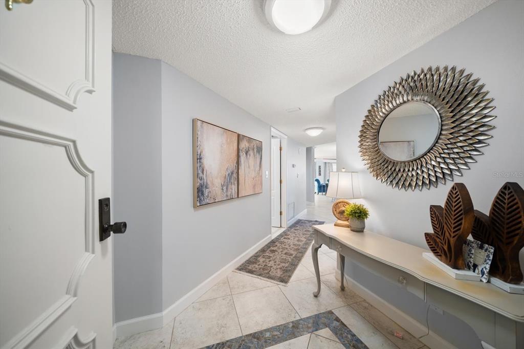 A hallway features light-colored tile flooring, a console table with decor, and a sunburst mirror — 1651 SAND KEY ESTATES COURT UNIT 28, CLEARWATER BEACH, FL
